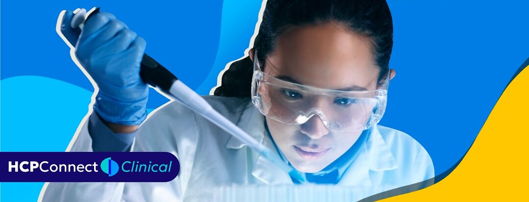 A woman with safety glasses uses a pipette to drop liquid into a test tube.